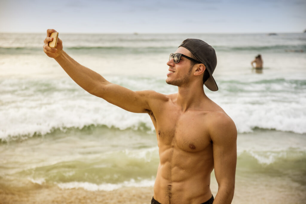 man with lean cut body on beach taking progress photos during a skinny fat workout plan